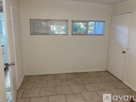 A room with tiled flooring and two windows with blinds.