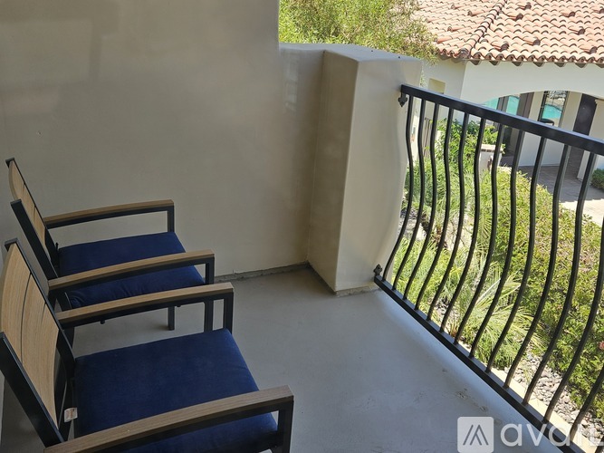 Two chairs are on a balcony with a view of a building with a tiled roof.