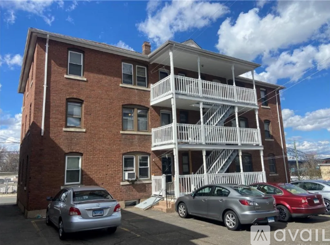 A two-story brick building with a white balcony on the second floor and cars parked in front.