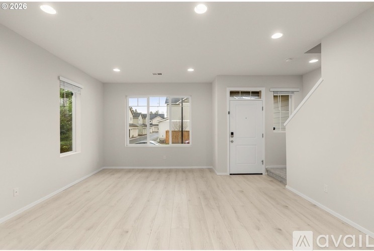 A spacious empty room with wooden flooring and white walls.