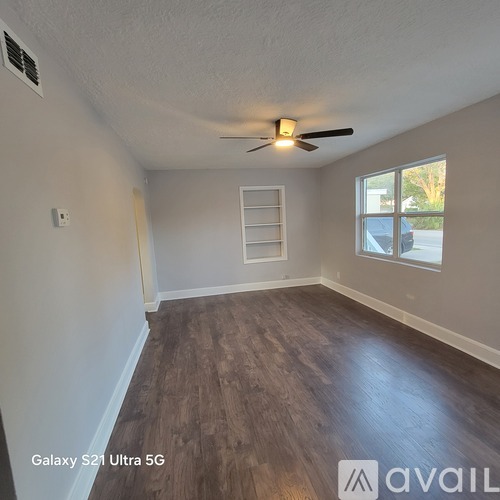 A room with a ceiling fan and a window with a ladder in the corner.