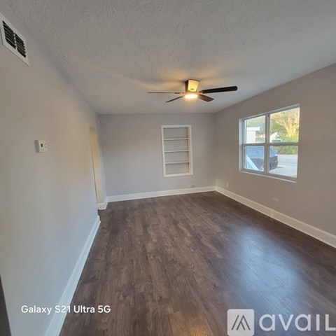 A room with a ceiling fan and a window with a ladder in the corner.