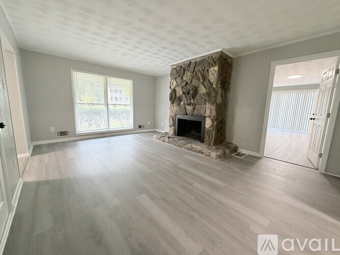 A spacious living room with a stone fireplace and hardwood flooring.