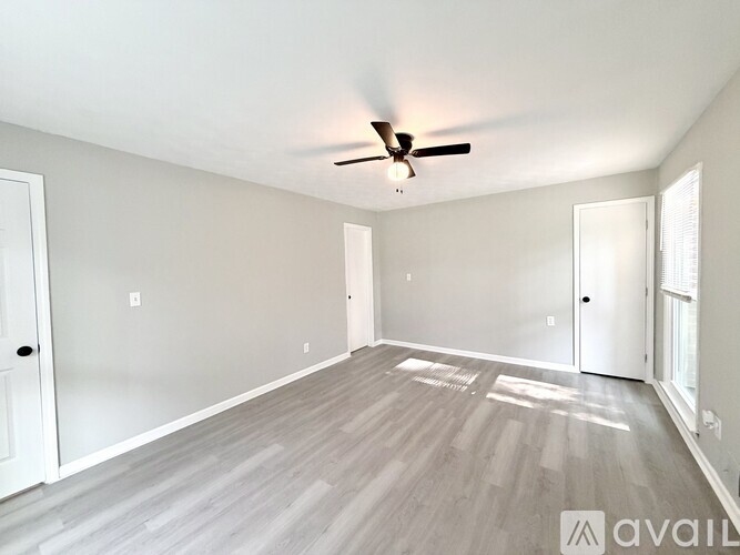 A spacious room with a ceiling fan and light, hardwood flooring, and white walls.