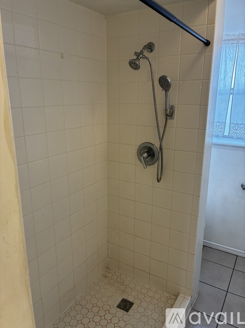 A white tiled shower with a black shower head and hand held shower.