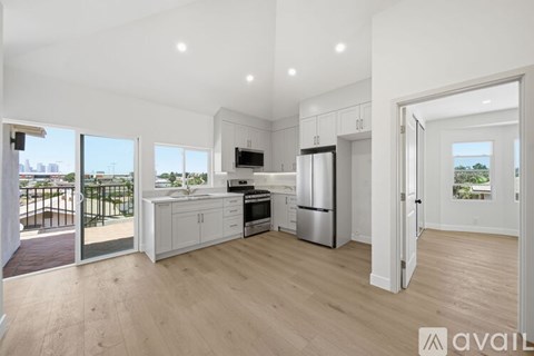 A modern kitchen with white cabinets and appliances, a wooden floor, and a balcony with a view of the city.