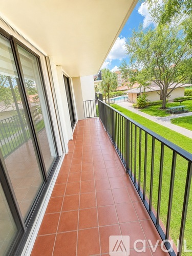 A balcony with a black railing and tiled floor overlooks a green lawn and trees.