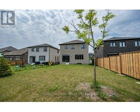 A tree stands in a grassy yard in front of a grey house.