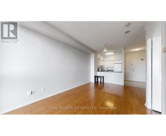 A spacious room with wooden flooring and white walls, featuring a small table and a window with blinds.