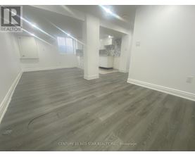 A spacious room with grey flooring and white walls, with a window on the left side.