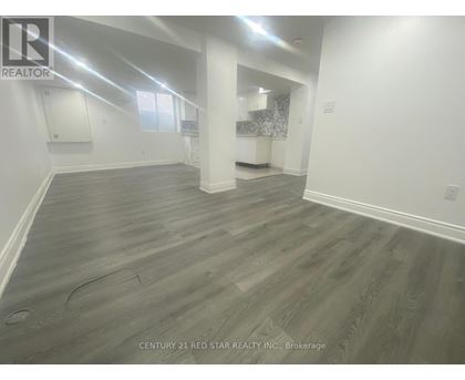 A spacious room with grey flooring and white walls, with a window on the left side.