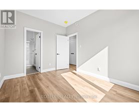 A room with wooden flooring and white walls, with a door on the right and a hallway leading to another room.