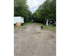 A dirt road with a white truck and a white trailer on the left and a black trash can on the right.