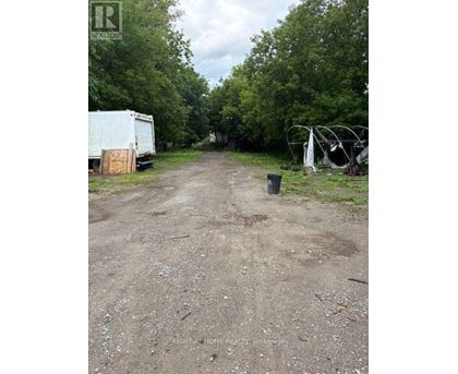 A dirt road with a white truck and a white trailer on the left and a black trash can on the right.