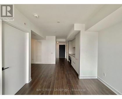 A spacious room with wooden floors and white walls, part of a Bay Street Group Inc. property.