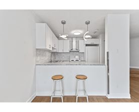 A kitchen with white cabinets and a white island with two stools.
