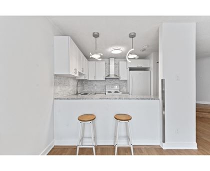 A kitchen with white cabinets and a white island with two stools.