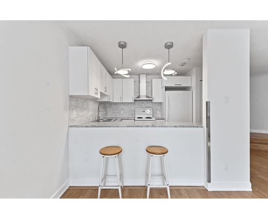 A kitchen with white cabinets and a white island with two stools.