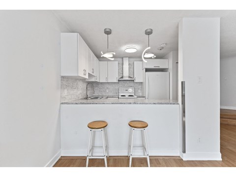 A kitchen with white cabinets and a white island with two stools.