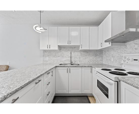 A kitchen with white cabinets and a marble countertop.