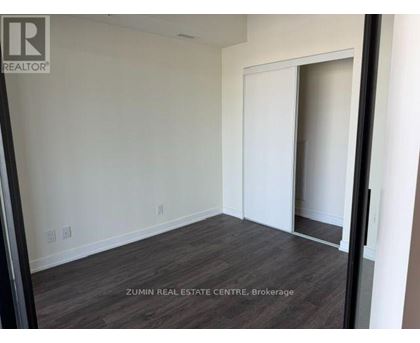 A room with a wooden floor and white walls, with a doorway leading to another room.