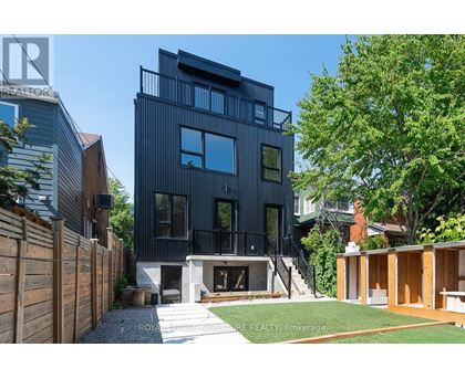 A modern black house with a balcony and a tree in front.