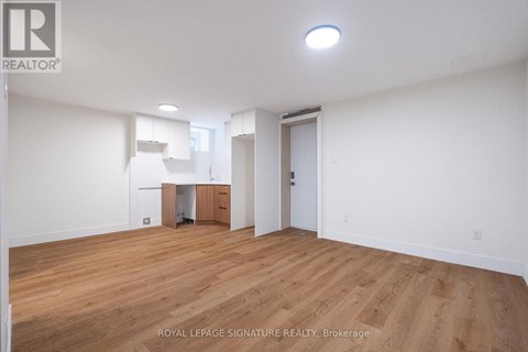 A room with wooden floors and white walls, with a small kitchenette in the corner.