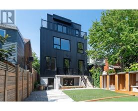 A modern black house with a balcony and a tree in front.