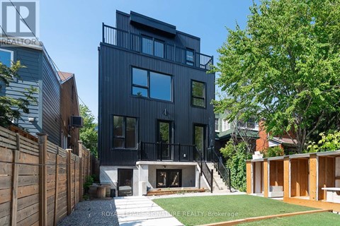 A modern black house with a balcony and a tree in front.