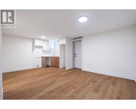 A room with wooden floors and white walls, with a small kitchenette in the corner.