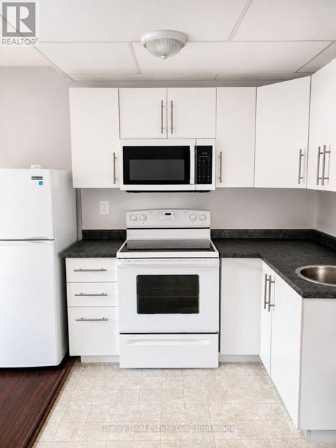 A white kitchen with a black countertop and a white fridge.