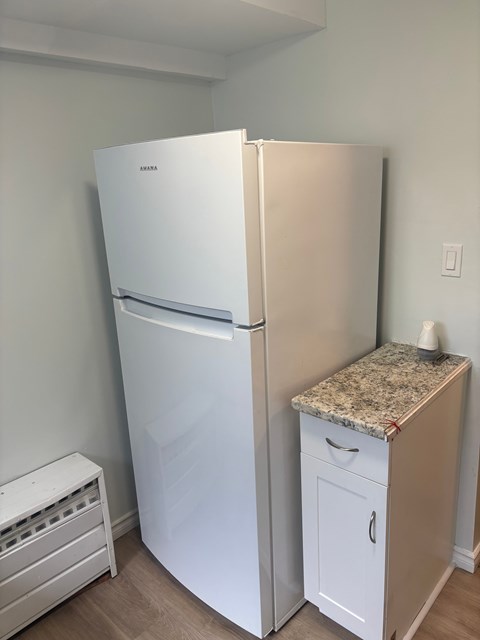 A white refrigerator and a small drawer cabinet with a granite countertop sit in a kitchen.