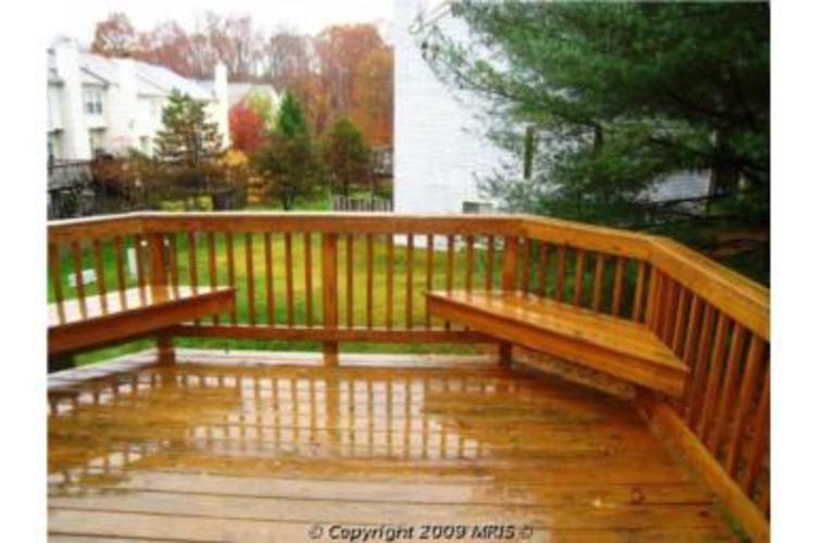 A wooden deck with a railing and a view of a lawn and trees.