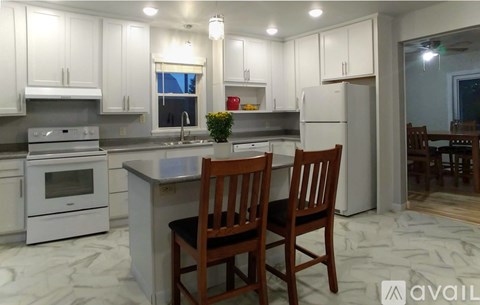 A kitchen with white appliances and wooden chairs.