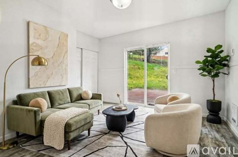 A living room with a green couch, a white chair, and a large painting on the wall.