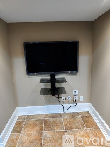 A black television is mounted on a wall above a black stand with a glass shelf.