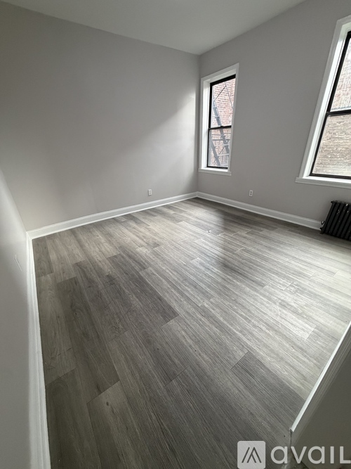 A room with wooden flooring and two windows.