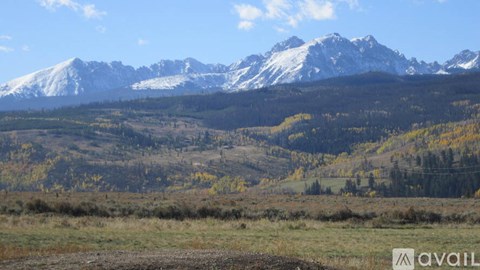 A mountain range with snow-capped peaks in the distance and a valley in the foreground with autumn-colored trees.