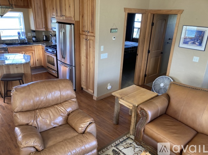 A living room with a brown leather couch and a kitchen area with a refrigerator and stove.