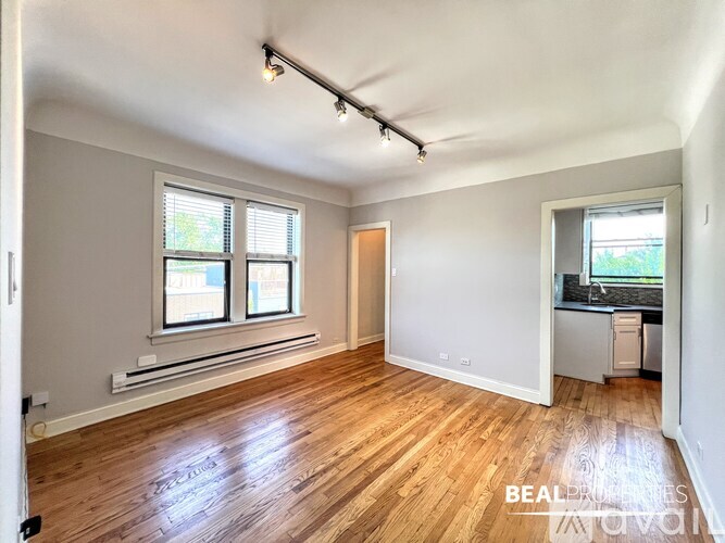 A room with wooden floors and white walls, with a window on the left and a door on the right.