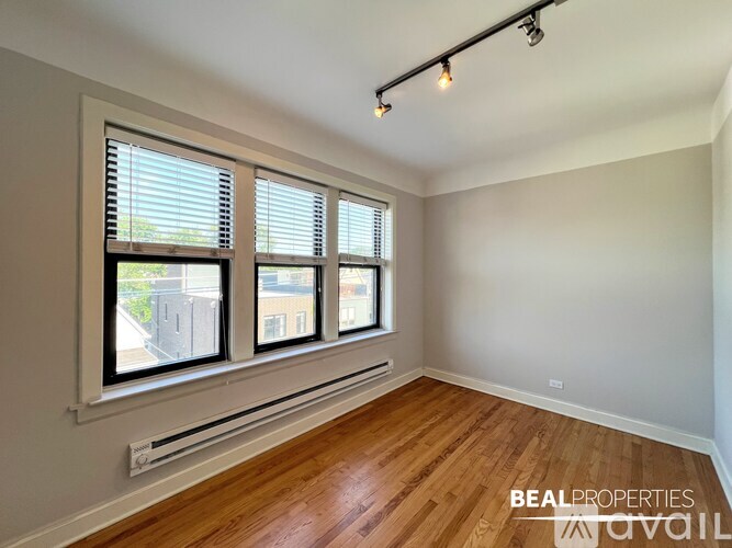 A room with wooden floors and two windows with blinds.