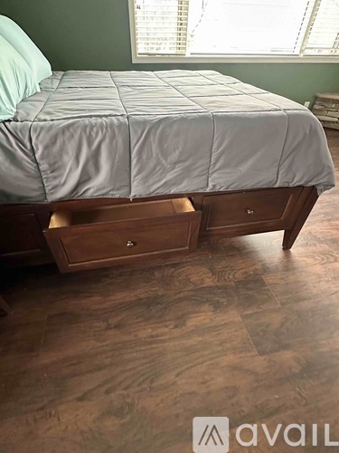 A bed with a grey cover and a wooden nightstand with two drawers.