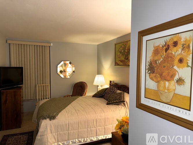 A bedroom with a bed, a television, a lamp, and a painting of sunflowers.