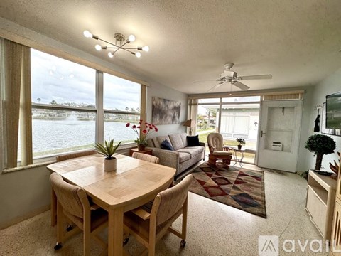 A living room with a dining table and chairs, a couch, a potted plant, and a ceiling fan.