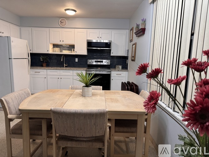 A kitchen with a table and chairs in the foreground and a staircase with flowers in the background.
