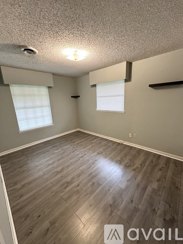 A room with wooden flooring and two windows.