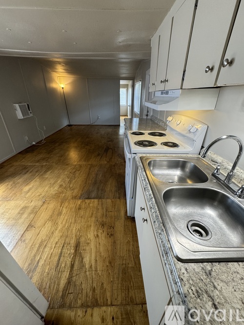 A kitchen with a stove, sink, and wooden floors.