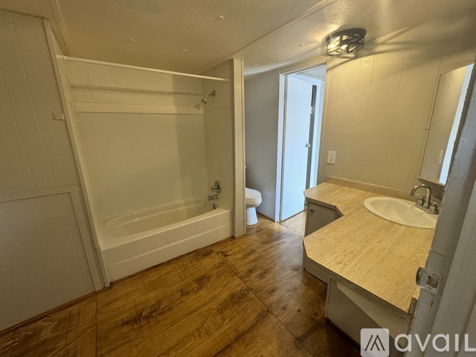 A bathroom with a white bathtub, sink, and wooden floor.