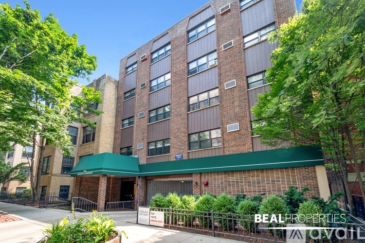 A multi-story brick building with a green awning and trees in front.