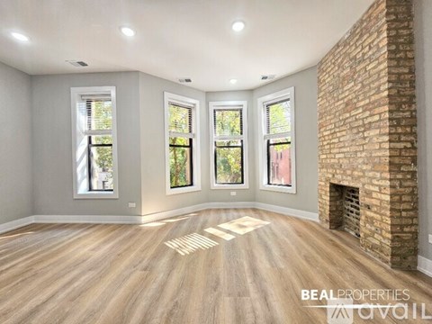 A spacious room with a brick fireplace and hardwood floors.